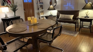 Ein Essbereich mit einem runden Holztisch, vier Stühlen und Kerzen. Im Hintergrund befinden sich ein Sofa und eine Lampe.