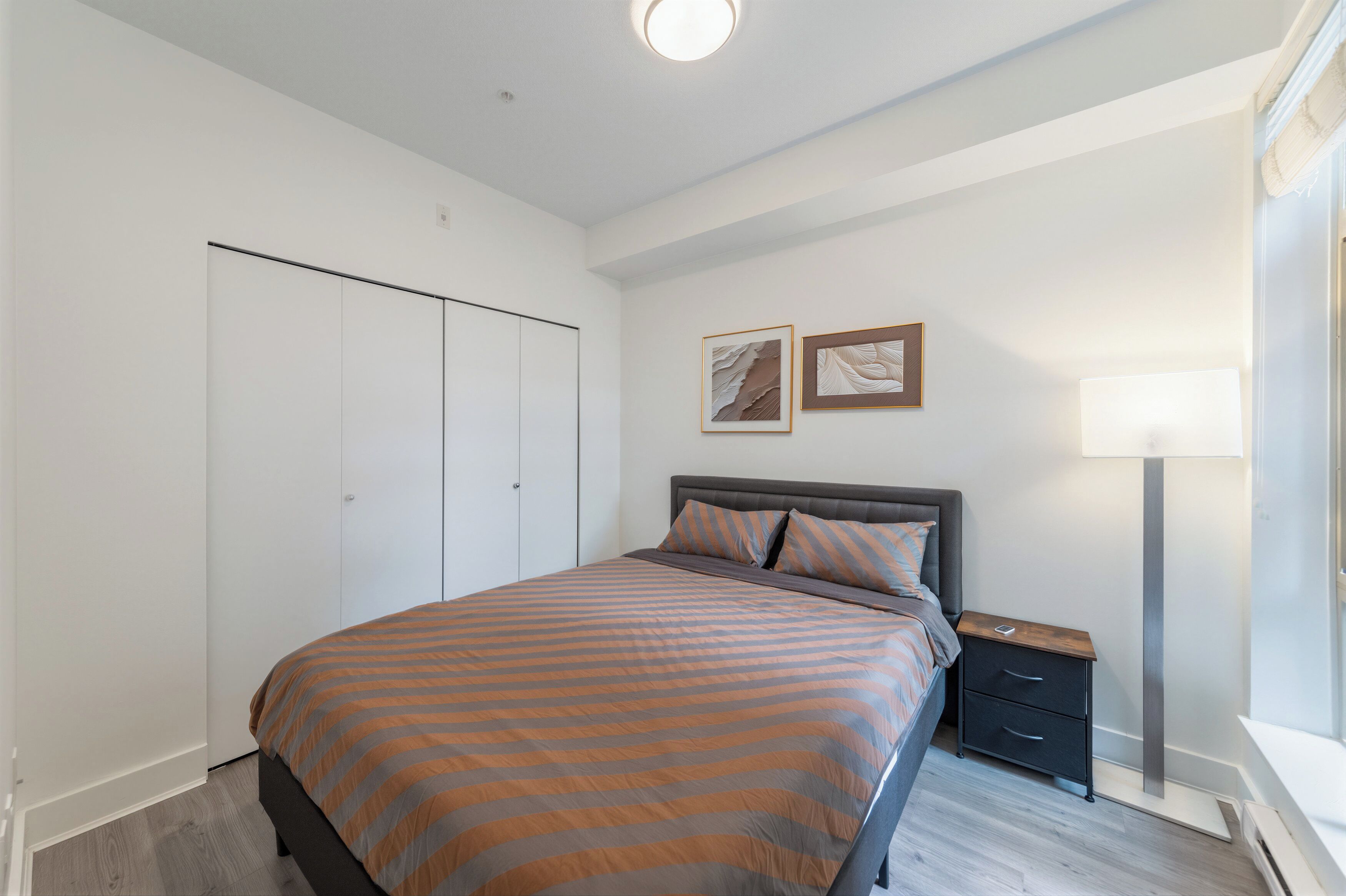 Una camera da letto con un letto, un comodino, una lampada da notte, un armadio e un'opera d'arte appesa al muro.