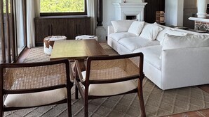 Een ruime woonkamer met een grote witte bank, een houten eettafel en een open haard.