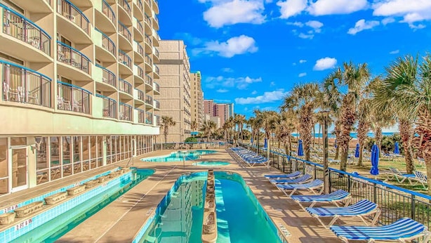 A hotel with multiple balconies, a swimming pool, and sun loungers.