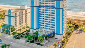 Ein Hotel mit einem zentralen Turm, einem Parkplatz und Blick auf den Strand.