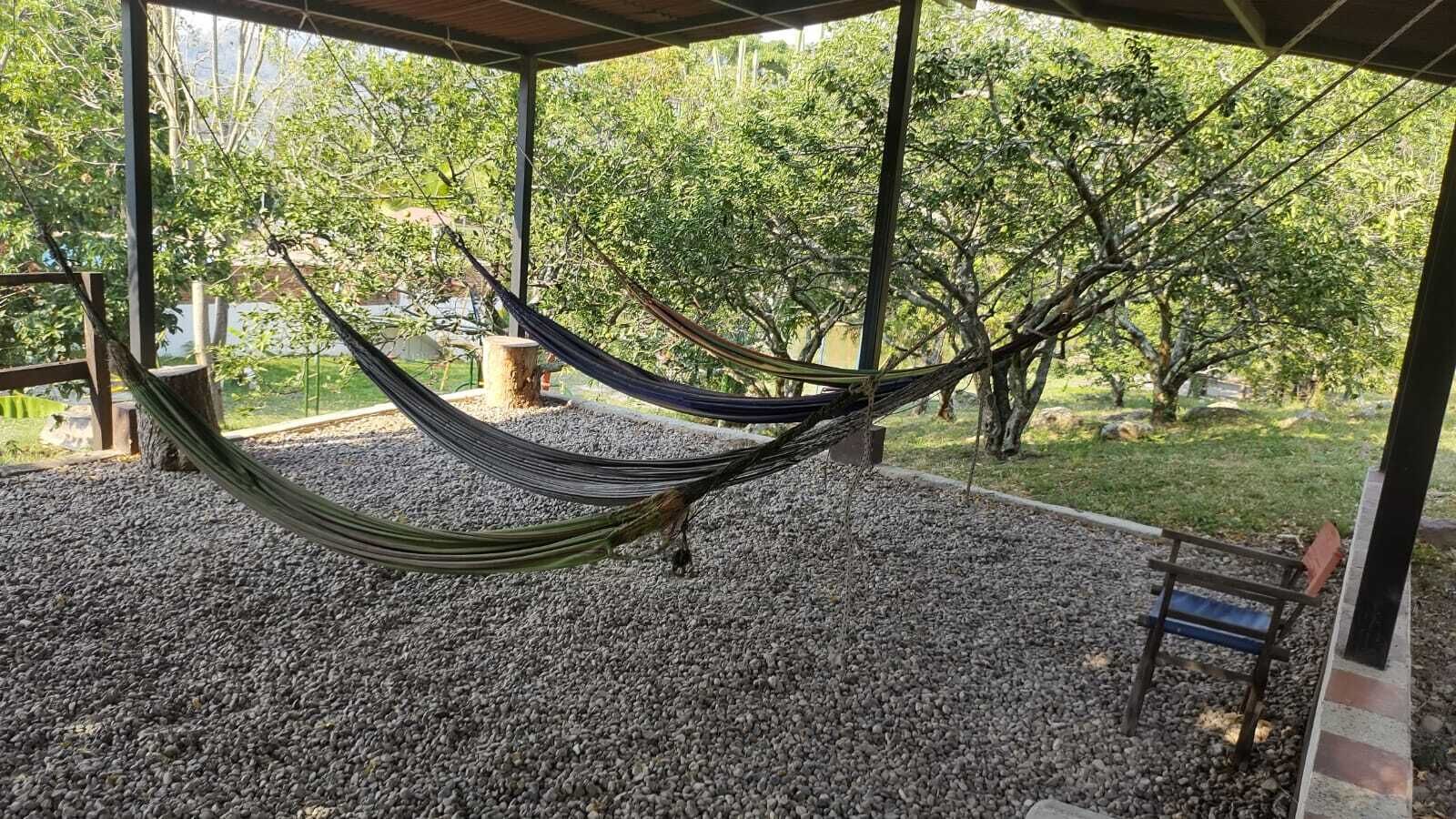 A hammock under a covered area with a gravel floor, surrounded by trees.