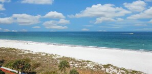 A beach with white sand, clear blue water, and scattered clouds.