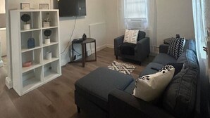 Un salon avec un ventilateur de plafond, un téléviseur fixé au mur, un canapé, une table basse et une bibliothèque.
