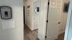 Un couloir avec un mur blanc, un détecteur de fumée et une porte donnant sur une autre pièce.