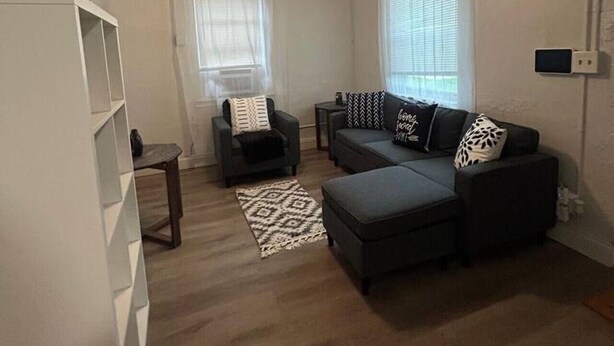 Un salon de taille modeste, doté d’un ventilateur de plafond, d’un ensemble de canapés, d’un fauteuil et d’une petite table.