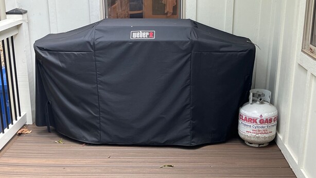Un barbecue couvert orné du logo Weber, une bouteille de propane et une terrasse en bois.