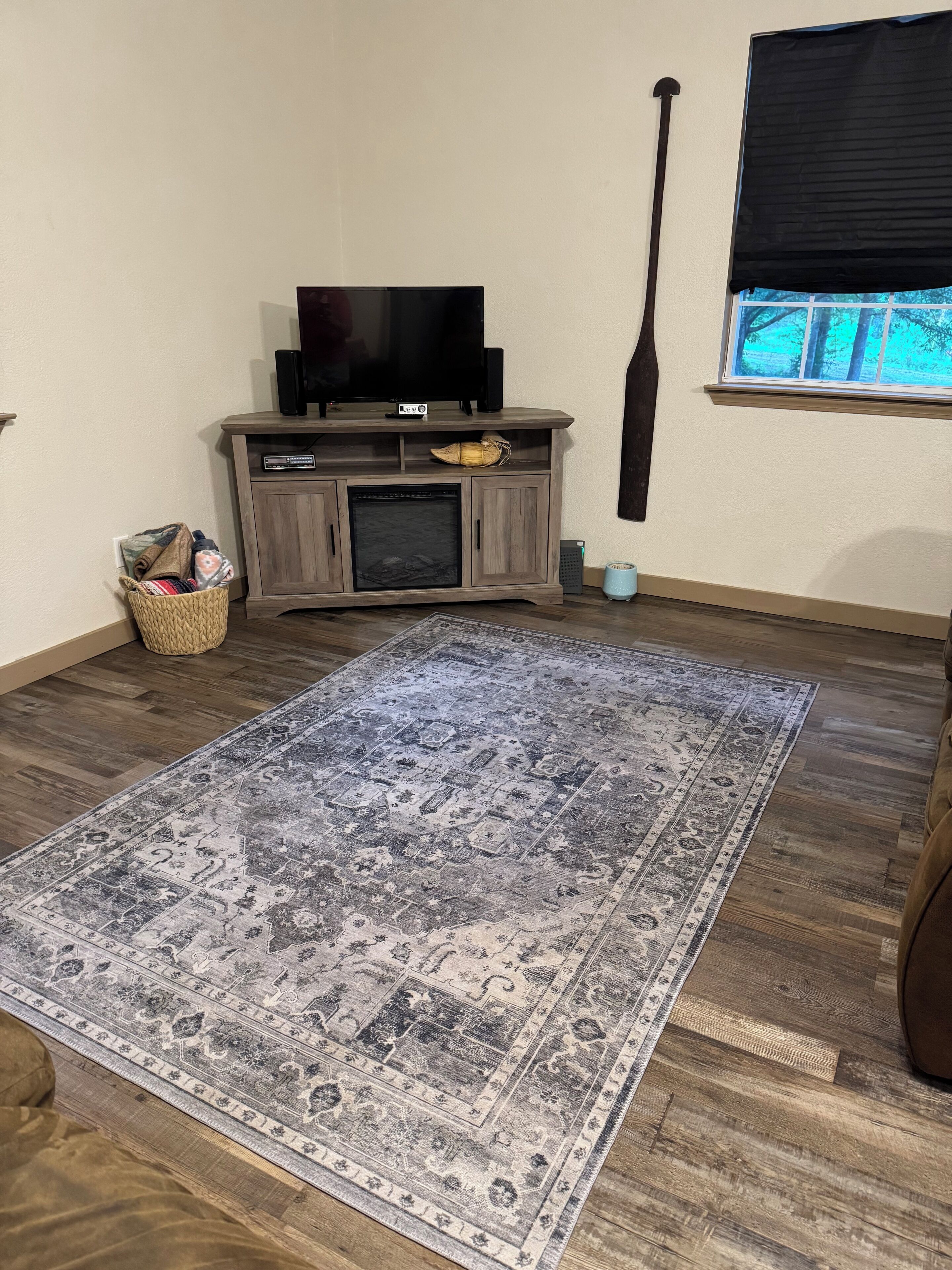 A living room with a large patterned rug, wooden entertainment unit, and a tall black object leaning against the wall.