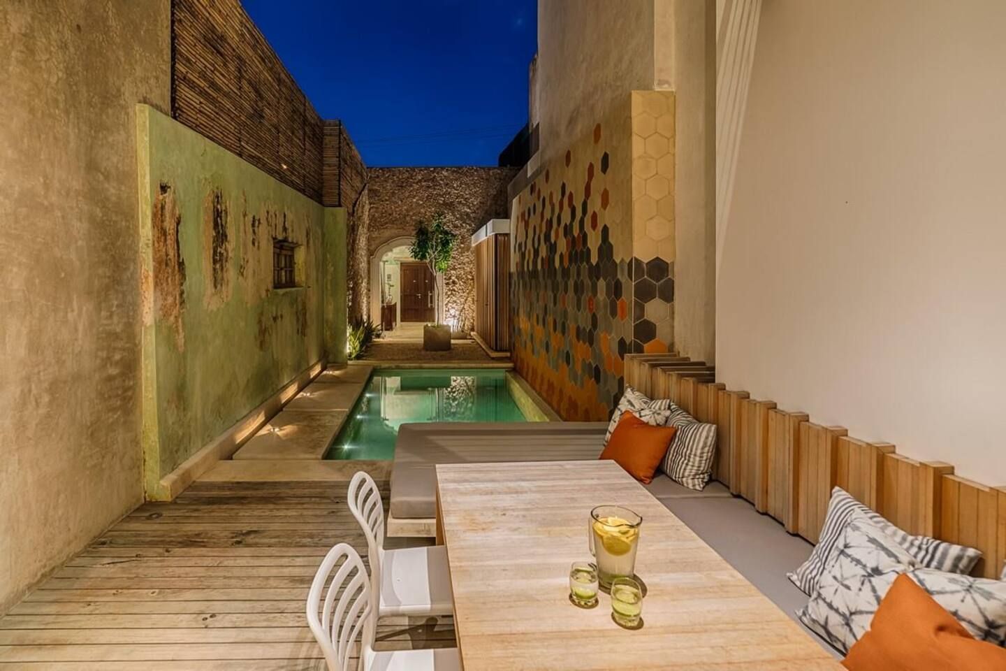 Ein schmales Innenhof mit Pool, Holzmöbeln und einem Tisch mit Getränken.