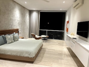A modern bedroom with a large bed, a TV, and a balcony with a view of the night sky.