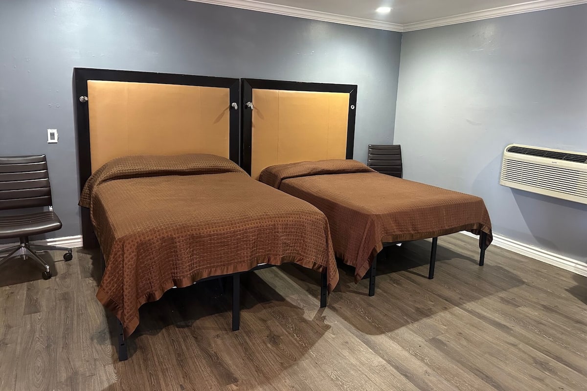 Ein Zimmer mit zwei Einzelbetten, einem Schreibtisch, einem Stuhl und einer Klimaanlage.