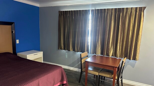A hotel room with a bed, a small desk, a wooden table, and a chair. - Driftwood Motel - Colton (Colton)