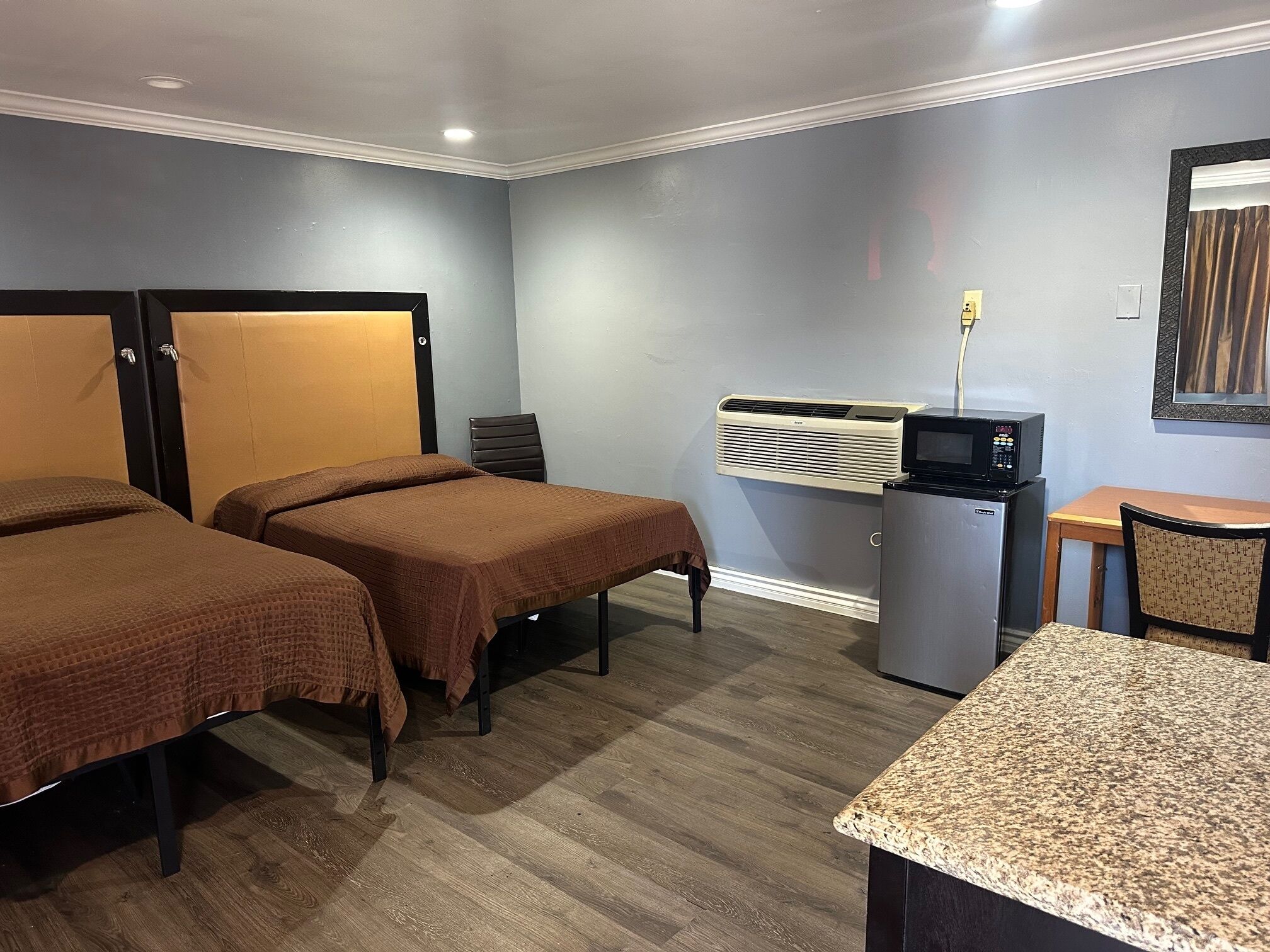 A hotel room with two single beds, a small desk, a microwave, and an air conditioning unit.