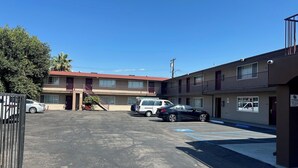 A multi-story motel with a parking lot, a gated entrance, and a sign indicating a pet-friendly policy. - Driftwood Motel - Colton (Colton)
