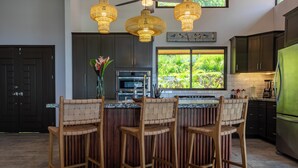 A kitchen with a central island, bar stools, a refrigerator, and a window with a view of greenery.