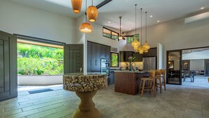 A modern kitchen with a central island, pendant lighting, and a view of greenery outside.