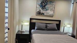 A neatly arranged bedroom with a bed, two bedside tables with lamps, a headboard, and a wall-mounted abstract painting. - Spacious 2BR modern living in Central Eastside location (Los Angeles)