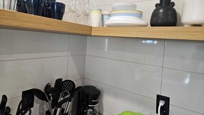 A kitchen with a wooden shelf holding various dishes and glasses, a coffee maker, and a green container. - Spacious 2BR modern living in Central Eastside location (Los Angeles)
