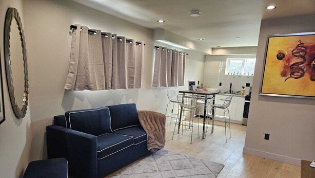 A modern living room with a dark blue sofa, a patterned rug, and a dining area with metal chairs and a table. - Spacious 2BR modern living in Central Eastside location (Los Angeles)