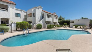 A swimming pool with a curved edge, surrounded by a paved deck. There are lounge chairs and a small staircase leading to a building with a tiled roof. - Modern Scottsdale Condo with Private Patio, Community Pool and Hot Tub (Scottsdale)