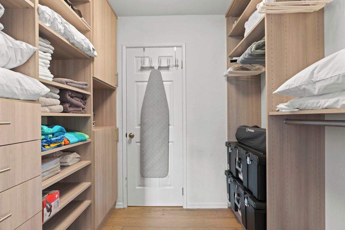 A narrow walk-through closet with shelves on both sides holding folded towels and pillows.