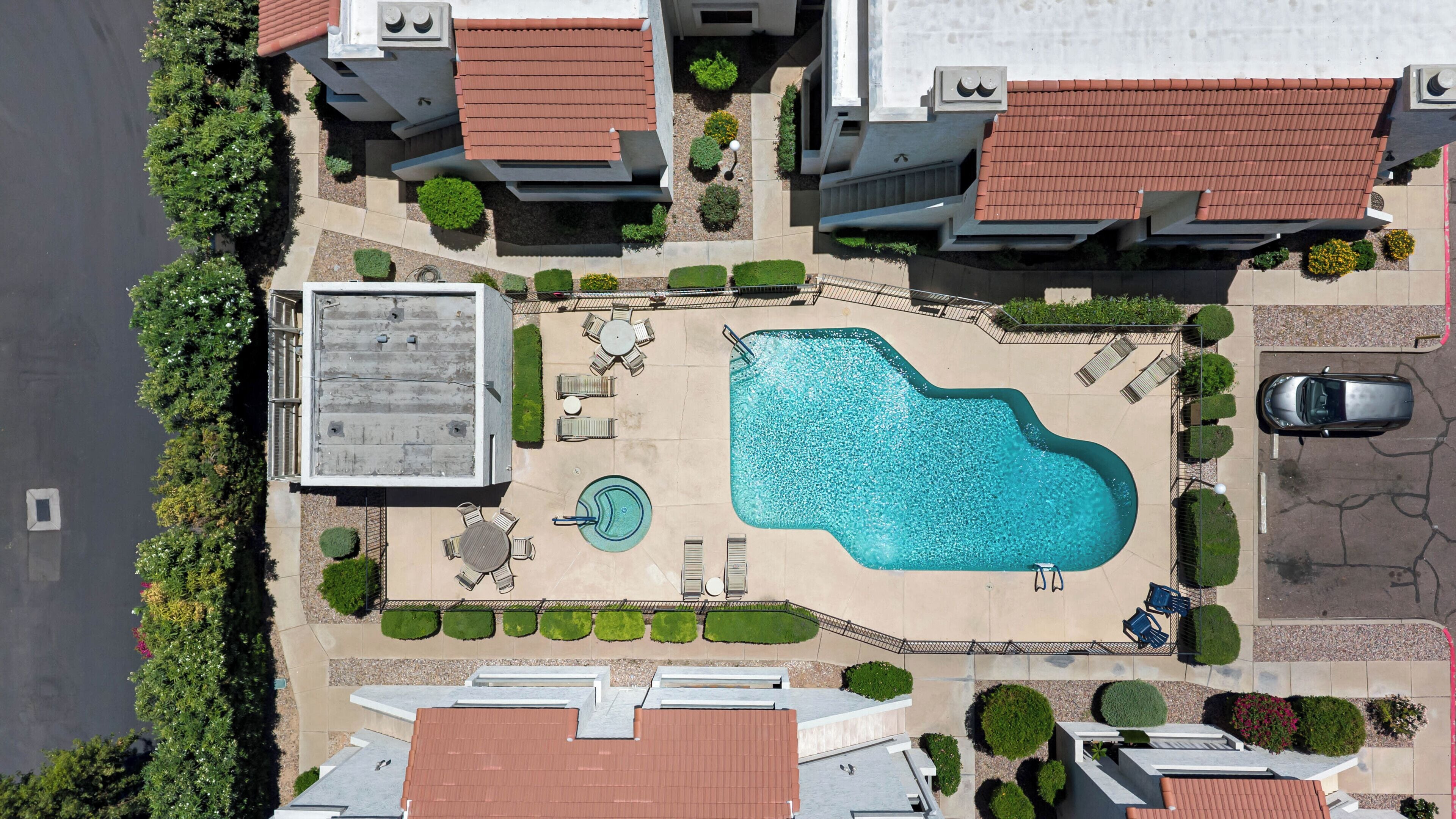 Vue aérienne d’un quartier résidentiel avec une piscine, un espace de détente extérieur et une voiture garée à proximité.