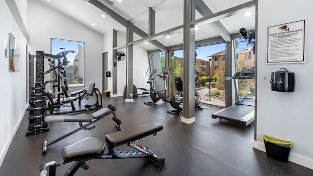 A modern gym with various exercise equipment, large windows, and a ceiling fan. - Woodland Springs with Community Pool, Hot Tub, Tennis, Sauna & Fitness Center C209 (Scottsdale)