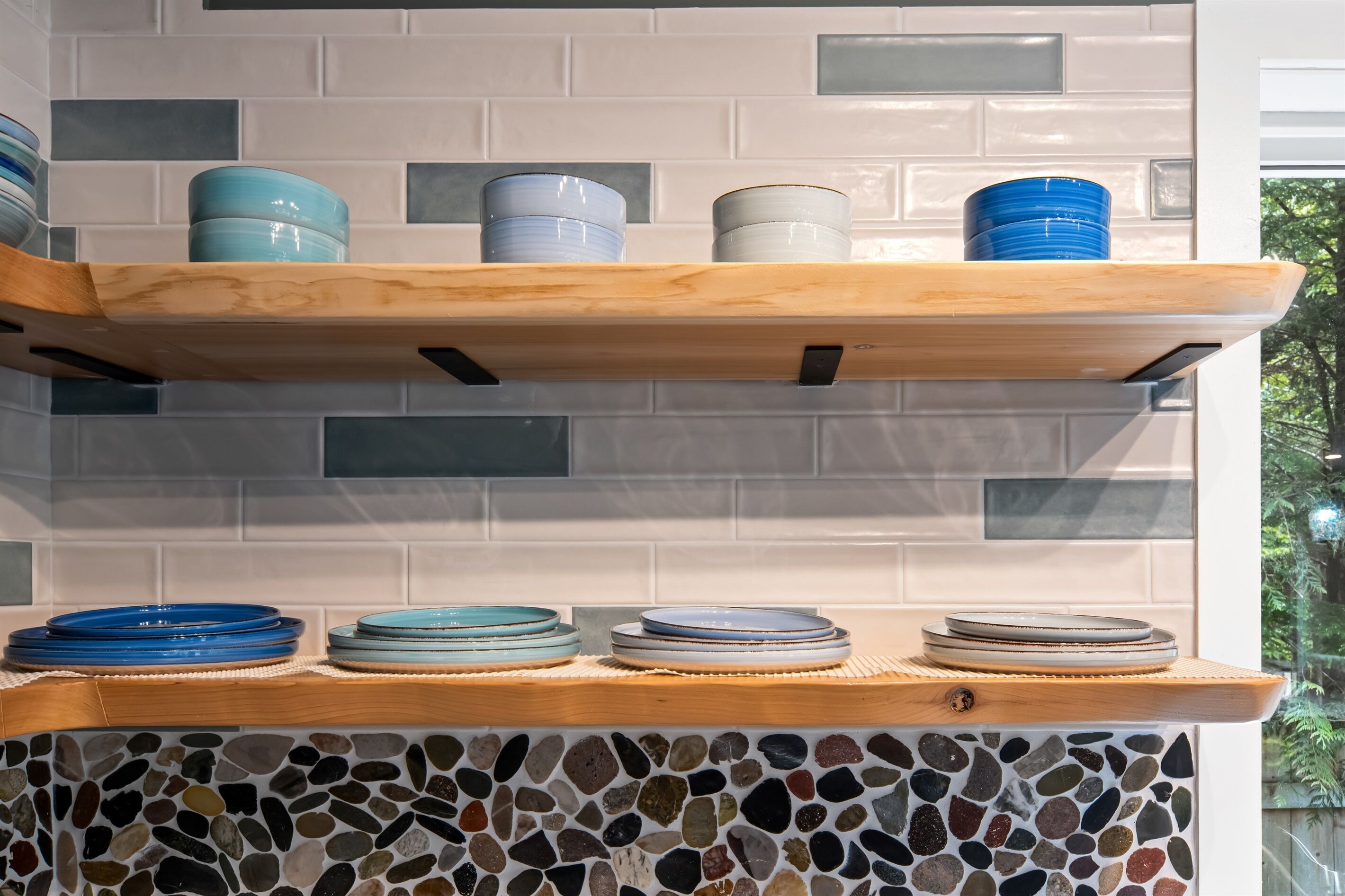 Een keuken met een houten plank waarop blauwe en witte borden en kommen staan, en een backsplash van mozaïektegels.