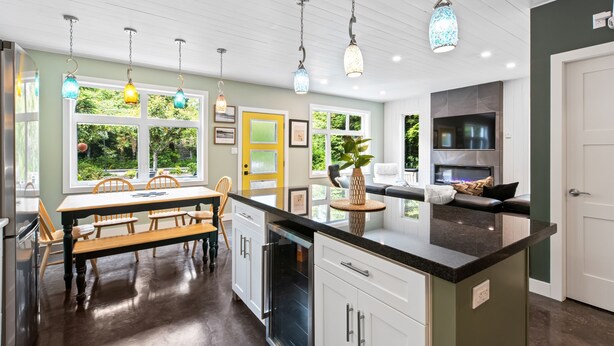 A modern kitchen with a central island, white cabinetry, and a dining area with wooden chairs and a bench.