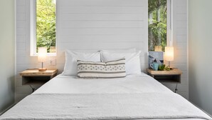 A bedroom with a large bed, two bedside tables with lamps, and a window with a view of trees.