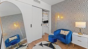 Moderni makuuhuone, jossa on geometrisesti kuvioitu tapetti, sininen nojatuoli, valkoinen yöpöytä ja vaatekaappi.