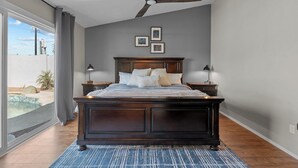 A bedroom with a dark wooden bed, a ceiling fan, and a view of a swimming pool through a large window. - Red Mountain Retreat - 4B/2B with Private Pool for your Arizona Getaway (Mesa)