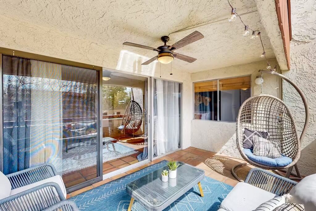 A sunlit patio with a ceiling fan, wicker furniture, and a glass door leading to an outdoor seating area.