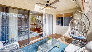 Une terrasse ensoleillée dotée d’un ventilateur de plafond, de meubles en osier et d’une porte vitrée donnant sur un espace extérieur aménagé pour se détendre.