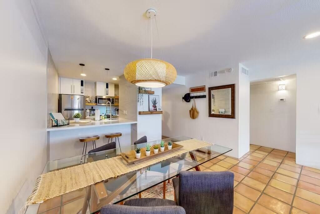 A modern kitchen with white cabinets, a stainless steel refrigerator, and a hanging light fixture.