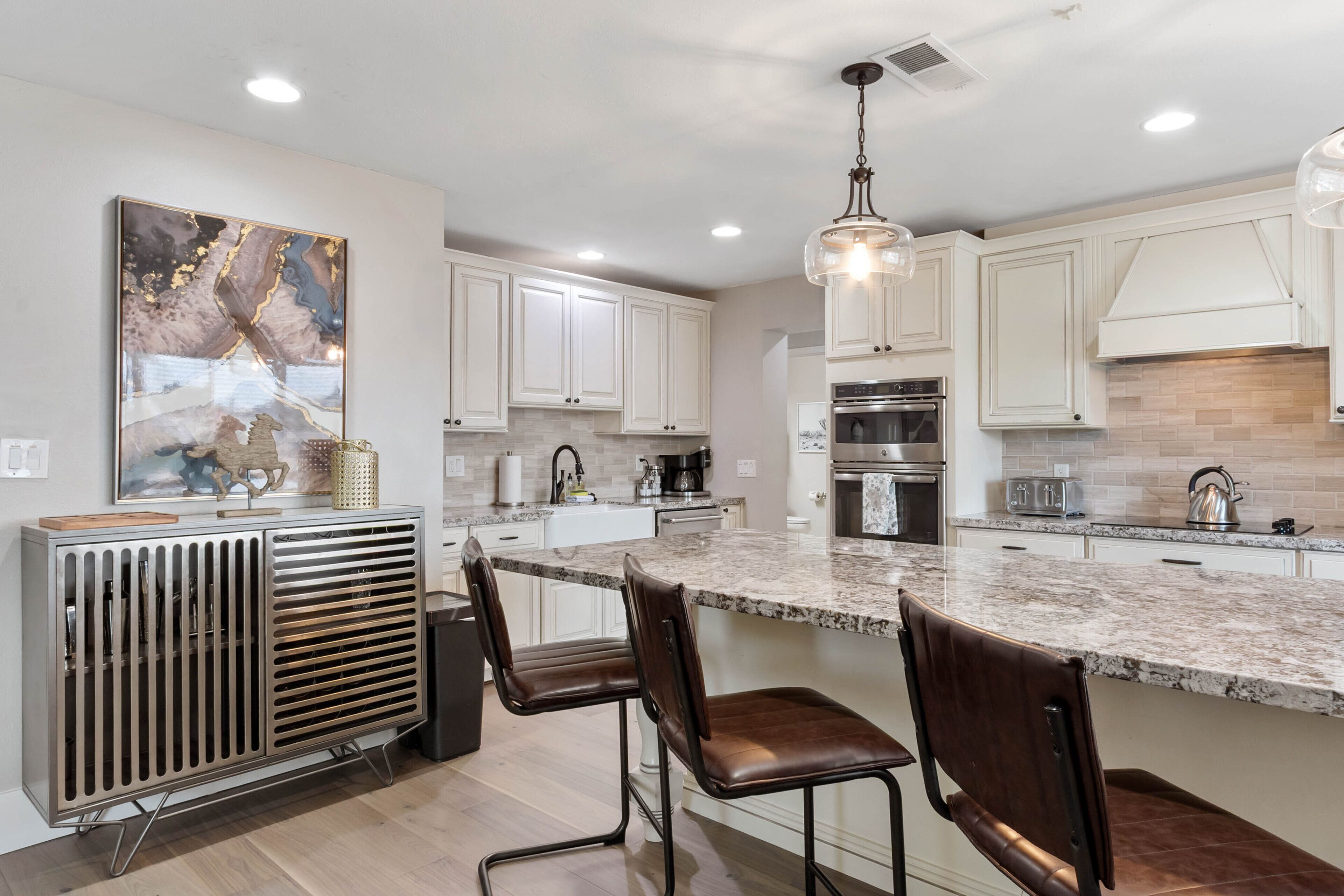 A modern kitchen with white cabinets, a granite countertop, and a hanging light fixture.