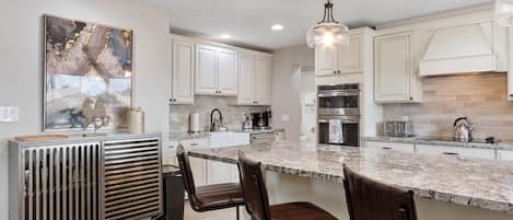 A modern kitchen with white cabinets, a granite countertop, and a hanging light fixture.