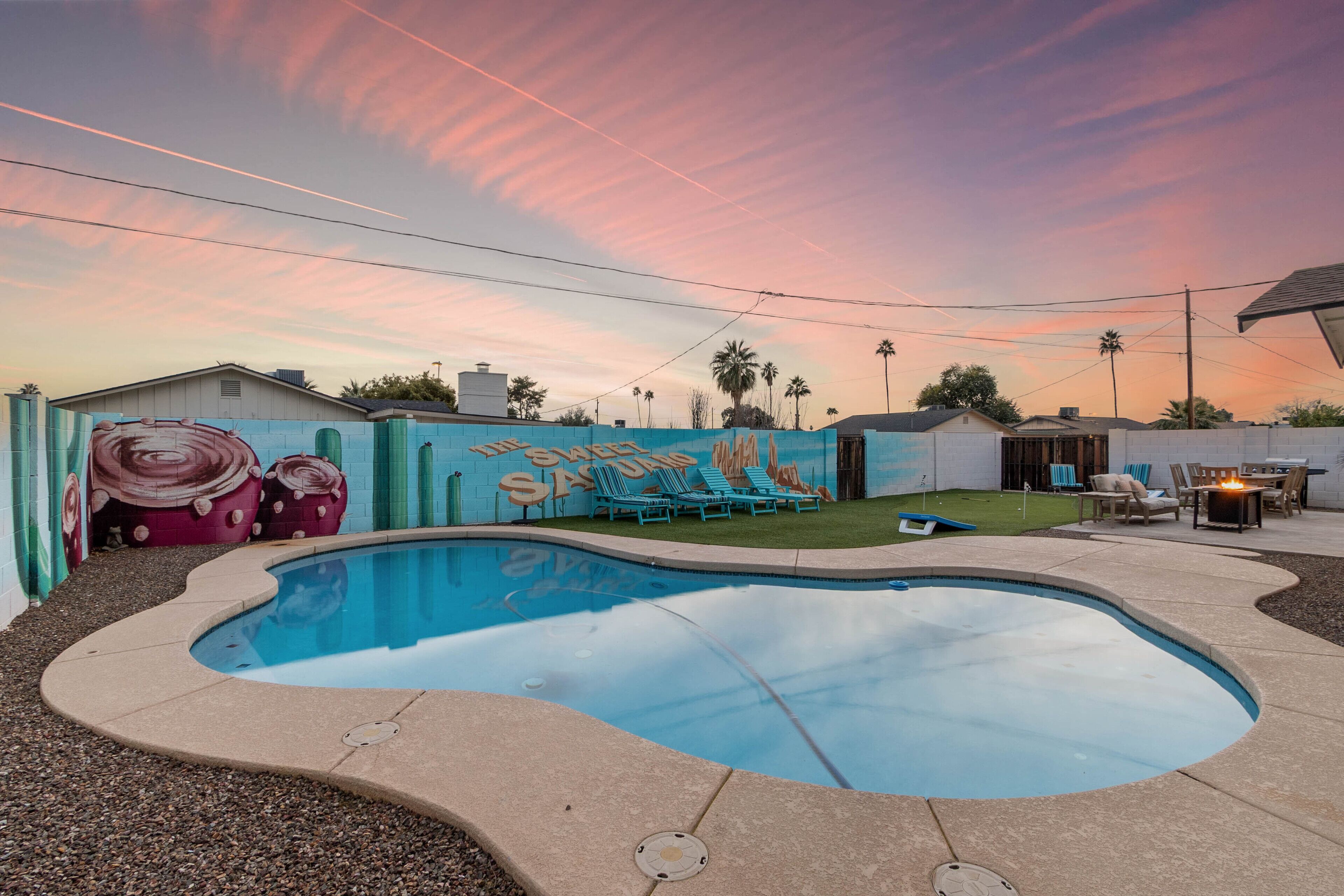 A swimming pool with a curved edge, surrounded by a patio area with lounge chairs and a small fire pit.