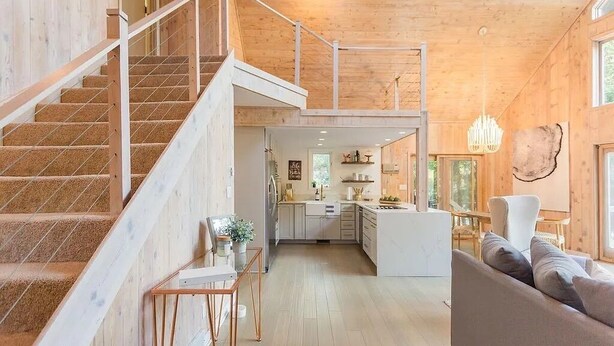 Een ruim interieur met een houten trap, een keukenhoek en een zithoek met een bank.