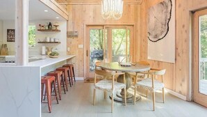 Een houten interieur met een ronde eettafel, witte rieten stoelen en een kroonluchter.