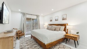 A bedroom with a wooden bed, a desk, a chair, a TV, and a window with curtains.