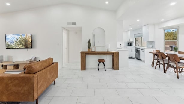 A spacious living area with a sofa, a wooden dining table, and a kitchen in the background.