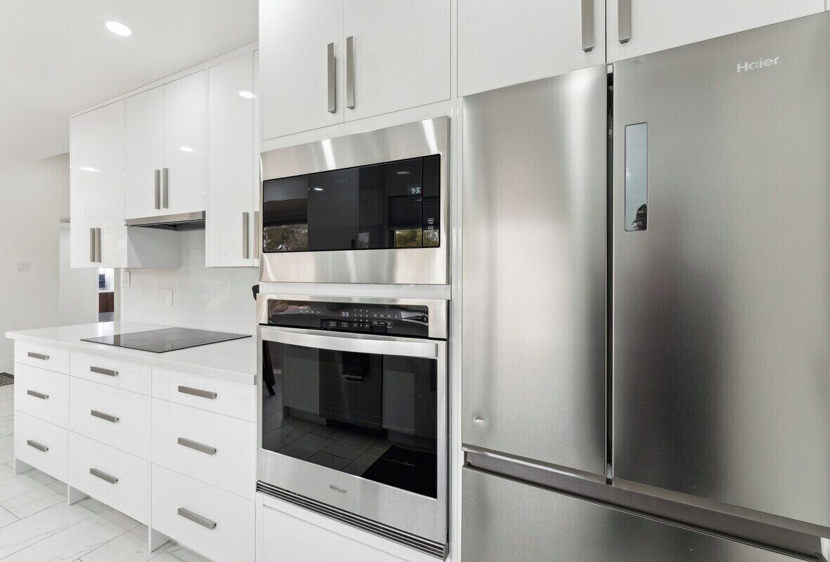 A modern kitchen with stainless steel appliances, white cabinetry, and a built-in oven.