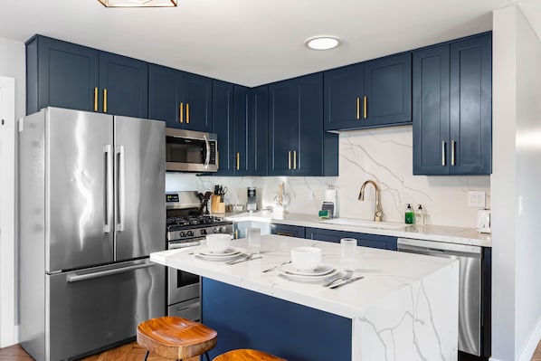 Cozinha moderna com armários azul escuro, eletrodomésticos de aço inoxidável e ilha de mármore.