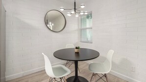 A room with a round table, four white chairs, a round mirror, and a modern chandelier.