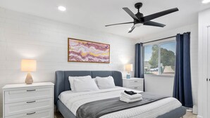 A modern bedroom with a bed, nightstands, a ceiling fan, and a large window with curtains.