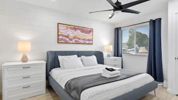 A modern bedroom with a bed, nightstands, a ceiling fan, and a large window with curtains.