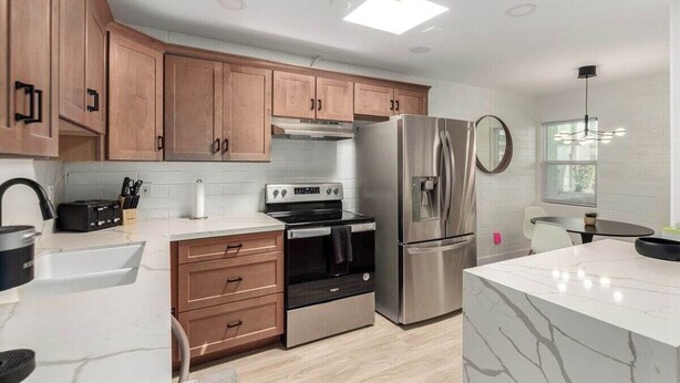 A modern kitchen with wooden cabinets, stainless steel appliances, and a marble countertop.