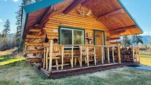A rustic log cabin with a porch, a green door, and a window. - Log Cabin Wilderness Lodge (Tok)
