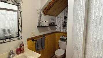 A bathroom with a wooden ceiling, a sink with toiletries, a toilet, and a mirror with a decorative frame.